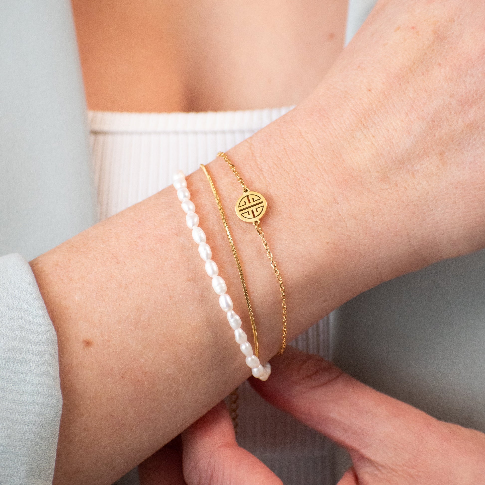 Close-up of a wrist wearing a gold bracelet with a circular design and a pearl bracelet.