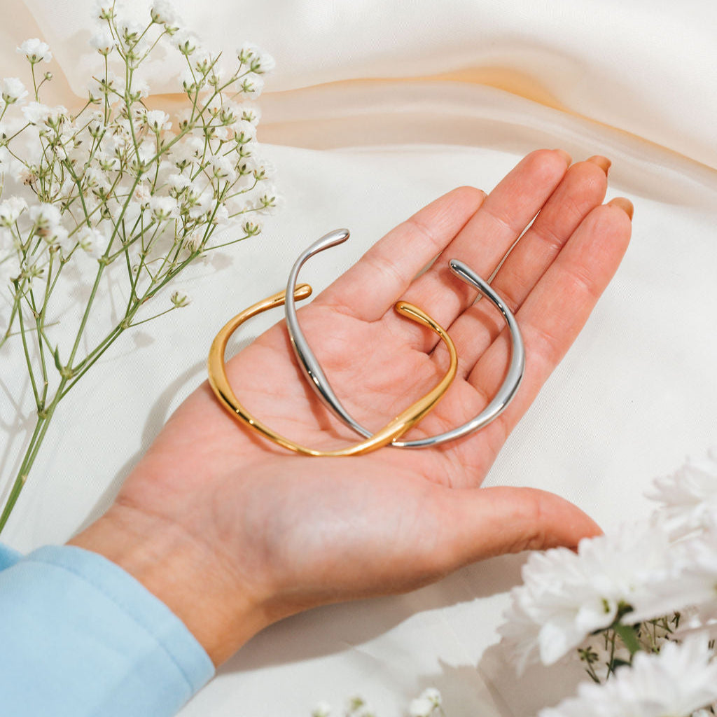 Hand holding two gold and silver bangles with a soft white background